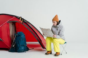 Woman in winter attire planning a camping trip with a map near a red tent.